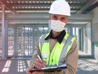 Construction worker in white hardhat and protective mask stands with clipboard opposite checkpoint...