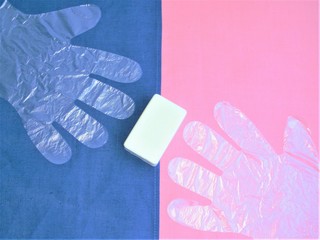 Composition of a piece of white toilet soap lying between two disposable gloves. Everything is on a linen background of blue and pink colors. View from above.