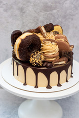 Peanut butter cake decorated with melted dark chocolate, donuts, chocolate bites, cake pops, macaroons and candies.