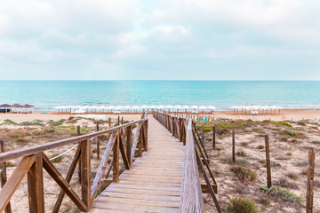 Fototapeta na wymiar wooden bridge over the protected dunes to access the beach umbrellas in Guardamar. Alicante, Spain