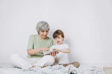 A little boy and his grandmother are having fun together against a light background