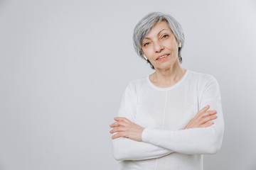 Elderly woman uses a mobile phone with hands free set, against a light background