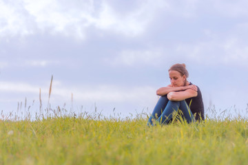 Naklejka na ściany i meble Sad girl sitting in the grass in the meadow