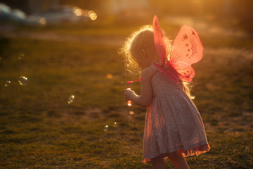 Fototapeta premium little girl plays with soap bubbles in a clearing at sunset at golden hour
