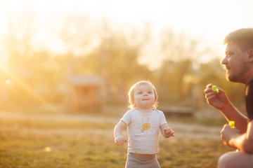 
dad and little son play with soap bubbles at sunset at golden hour