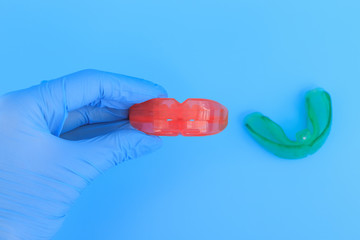 Doctor's hand in a blue glove holds a myofunctional trainer for teeth correction. Blue background. Selective focus.
