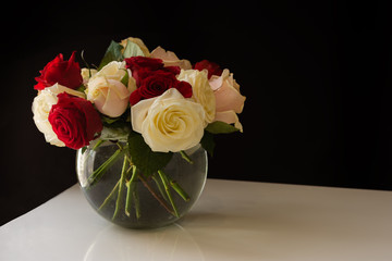 Roses in a glass vase on a black background. A bouquet of different flowers of roses on the table. A holiday bouquet. White and red roses