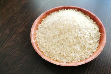 Parboiled rice on a bamboo bowl on wood table with copy space on the left side.  Selective focus.