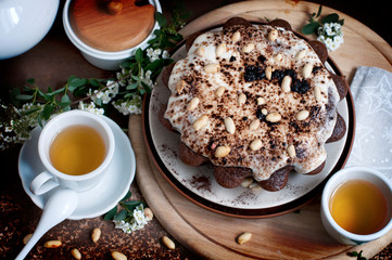 Chocolate cake with peanuts on table with tea and flowers on dark brown background. Top view