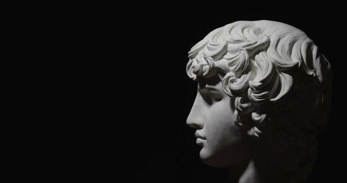 Epic studio shot of rotating Antinous gypsum head with moving and changing  lighting. The play of light and shadow on half the face of statue of man. On black background isolated 4k