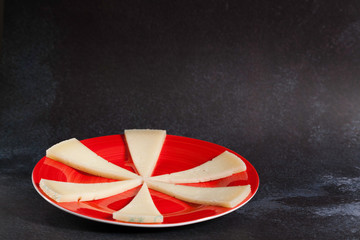 six slices of typical spanish manchego cheese on red ceramic plate