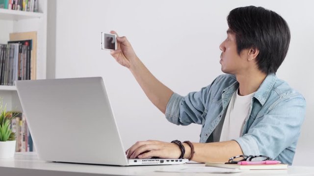 Asian Casual Businessman or Freelancer Working From Home by Laptop and Selfie by Smartphone. Casual Businessman or Freelancer in happy and enjoy emotion