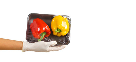 Gloved hand holding packed bell peppers. Red and yellow sweet peppers in plastic food wrap on palm....