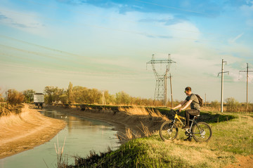 A man on a Bicycle stands on the Bank of the canal and looks into the distance. Travel, healthy lifestyle
