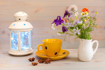 Still life, a white lantern, a yellow mug on a saucer, flowers in a white jug, and a Badian on the table. Morning tea