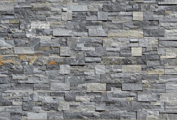 Grey stone wall cladding made of strips and square blocks stacked . Background and texture. 