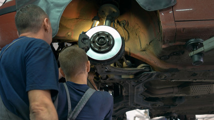 Two mechanics repairing old car hub breakers. Bottom of an old lifted car in a service center.