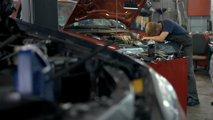 Professional mechanic repairing car in a service center. Cars with opened hoods.