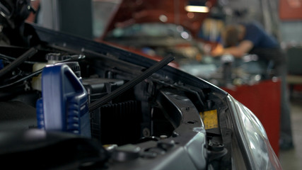 Professional mechanic repairing car in a service center. Cars with opened hoods.