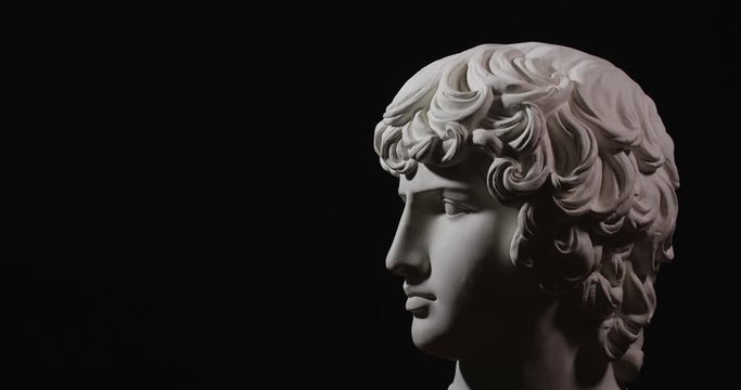 Epic studio shot of rotating  gypsum head with dramatic  lighting. The play of light and shadow on half the face of statue of man. On black background isolated 4k