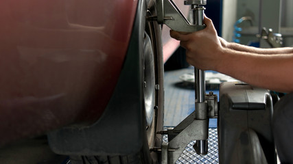 Engineer is setting camber caster gauge for checking alignment of tire. Close-up mechanic hands and car tool.