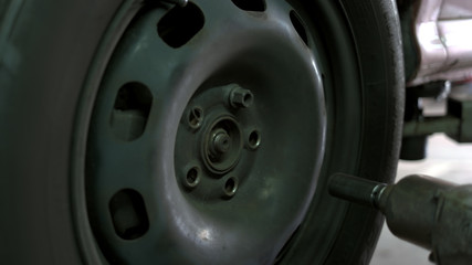 Close up man unscrewing car wheel. Removing nuts using electrical screwdriver.
