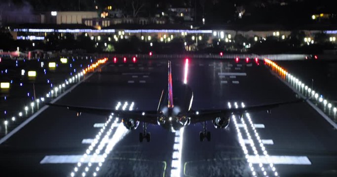 Night Footage Of A Plane Landing On The Runway At San Diego International Airport Colorfully Illuminated With Red, Green, White And Blue Lights. Night Cityscape Is Seen On The Background. 4K