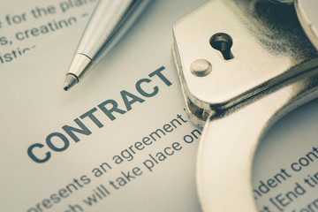 Pen and a handcuff on a legal contract form, depicting a contract was signed by a coerced or forced...