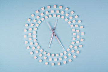 Circle of refined sugar and insulin syringes on blue background. Type 2 diabetes. Dose of insulin...