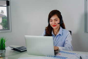 Happy asien young business woman wearing wireless headphones, looking at computer screen, waving hello. Pleasant attractive mixed race female professional holding video call with client.