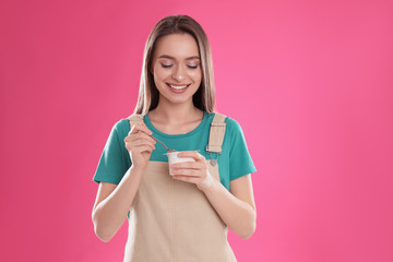 Young attractive woman with tasty yogurt on pink background