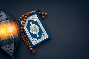 Holy Al Quran with written arabic calligraphy meaning of Al Quran, lantern lamp and rosary beads or...