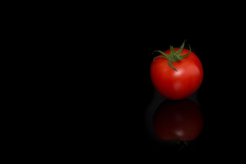 Single real tomatoe seen at its top on a black background with reflection
