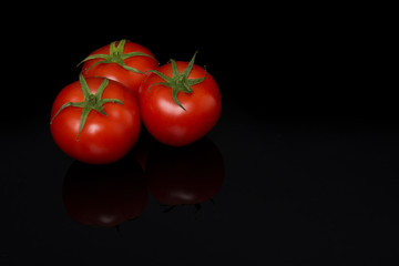 Three real tomatoes in a triangle on a black background with reflection