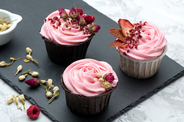 Pink cupcakes decorated by sublemented berries  and buttons of dry flowers on stone board with textile napkin