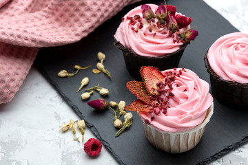 Pink cupcakes decorated by sublemented berries  and buttons of dry flowers on stone board with textile napkin