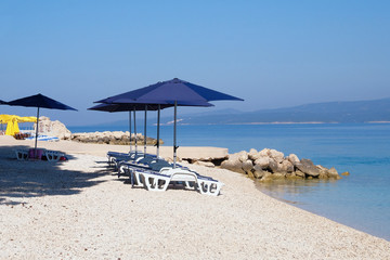 Fototapeta na wymiar Blue beach umbrellas and chaise for relax and comfort on sea resort. Summer vacations and travel for seaside. Paid service on comfort beaches.