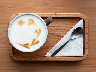 a wooden tray with a Cup of cappuccino, napkin and spoon is placed on a wooden table. close up. the view from the top.