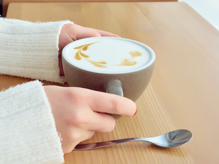 A girl is sitting in a cafe. Drinking Coffee. Gray cup with coffee. Holds a cup of coffee in his hand. Close-up