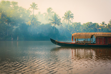 A traditional house boat is anchored on the shores of a fishing lake in the palm tree jungle at...