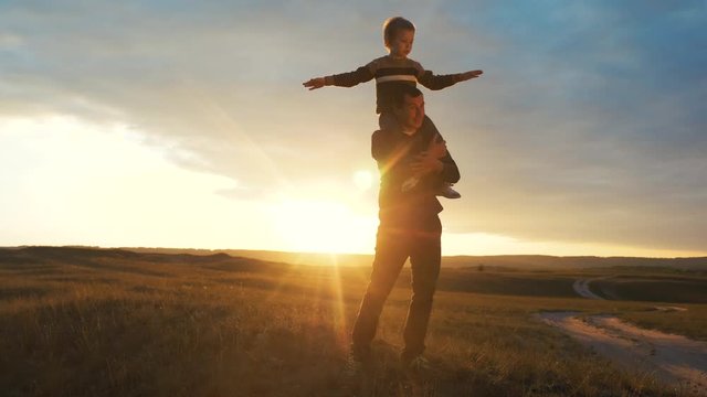 happy family. son sits on his neck teamwork at father shows hands to the side plays at the pilot depicts an airplane silhouette at sunset. happy family concept childhood man dad with little boy son