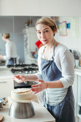 A middle aged woman pastry chef or baker prepares a cake and decorates it with icing.