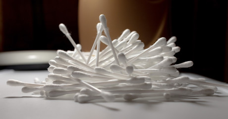 white soft cotton ear sticks are stacked in a small pile on a white surface. the container is visible in the background. soft shadows and pleasant light