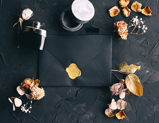 stylish black envelope in a composition with flowers, perfume and a flash drive