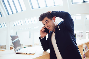 Young experienced businessman in suit having mobile phone conversation asking about troubles with...