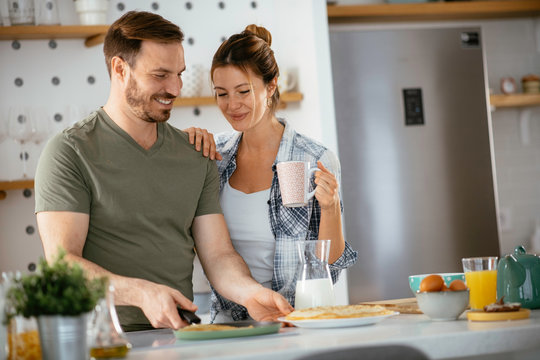 Young couple making pancakes at home. Loving couple having fun while cooking.	