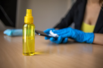Woman's hand in blue gloves sanitizing cleaning smartphone mobile phone with alcohol on wood table surface with wet wipes
