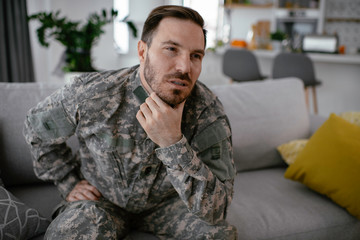 Fototapeta premium Depressed soldier sitting on sofa in living room. Young marine having PTSD. 
