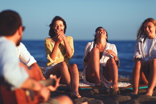 Small group of young people sitting on the beach and laughing
