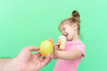Fototapeta na wymiar little girl 4 years old in a pink T-shirt on a green background emotionally repels the proposed lemon, chooses ice cream